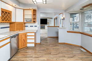 Kitchen featuring stainless steel dishwasher, tile counters, light hardwood / wood-style flooring, and tasteful backsplash