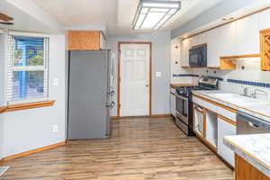 Kitchen with decorative backsplash, light wood-type flooring, white cabinetry, and stainless steel appliances