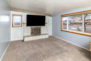 Unfurnished living room with a fireplace, carpet floors, and a textured ceiling