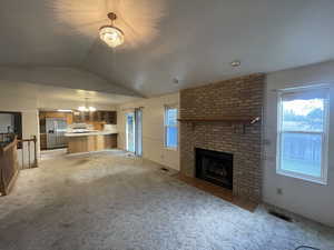 Unfurnished living room featuring a brick fireplace, a notable chandelier, light carpet, and vaulted ceiling