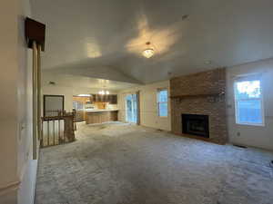 Unfurnished living room with a fireplace, carpet flooring, a chandelier, and vaulted ceiling