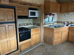 Kitchen with exhaust hood, backsplash, black electric range oven, and sink