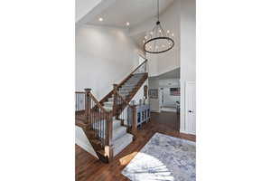 Stairway featuring wood-type flooring, a towering ceiling, and a notable chandelier