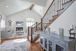 Stairs with beamed ceiling, high vaulted ceiling, wood-type flooring, and a high end fireplace