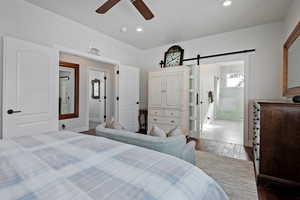 Bedroom featuring hardwood / wood-style floors, a barn door, ensuite bath, and ceiling fan