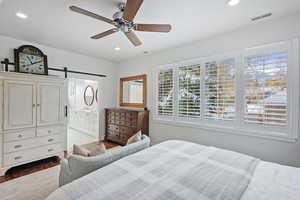 Bedroom with connected bathroom, a barn door, ceiling fan, and light wood-type flooring