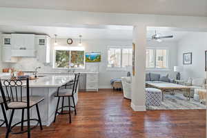 Kitchen featuring white cabinetry, dark wood-type flooring, decorative light fixtures, a kitchen bar, and custom exhaust hood