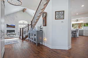 Interior space featuring a large fireplace, hardwood / wood-style floors, lofted ceiling with beams, and a notable chandelier