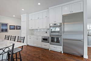 Kitchen with stainless steel appliances, light stone counters, dark hardwood / wood-style flooring, backsplash, and white cabinets