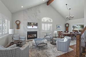 Living room with beam ceiling, dark hardwood / wood-style flooring, high vaulted ceiling, a chandelier, and a fireplace