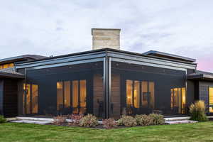 Back house at dusk with a yard and a sunroom