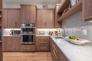 Kitchen with double oven, light stone countertops, sink, and light wood-type flooring