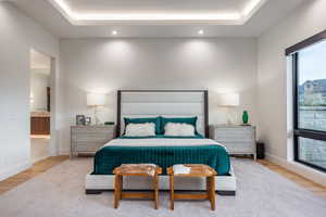 Bedroom with a raised ceiling, connected bathroom, and light hardwood / wood-style flooring