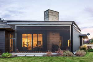 Back house at dusk with a yard and a sunroom