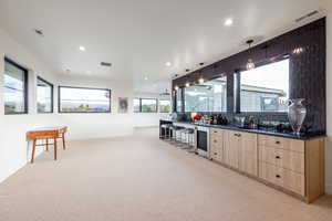 Kitchen featuring pendant lighting, light brown cabinets, light colored carpet, and beverage cooler