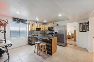 Kitchen featuring appliances with stainless steel finishes, backsplash, a center island, a breakfast bar area, and light tile patterned flooring