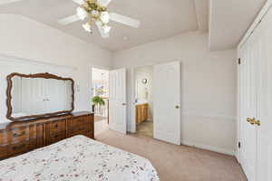 Bedroom featuring light carpet, ensuite bathroom, ceiling fan, and lofted ceiling