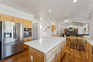 Kitchen featuring appliances with stainless steel finishes, ornamental molding, ceiling fan, dark wood-type flooring, and a kitchen island