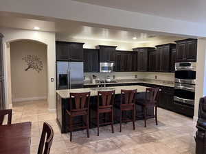 Kitchen featuring sink, light stone counters, a breakfast bar, a center island with sink, and appliances with stainless steel finishes