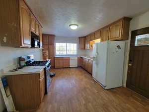 Kitchen with a textured ceiling, hardwood / wood-style floors, and white appliances