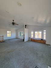 Carpeted empty room with a textured ceiling, vaulted ceiling, and ceiling fan