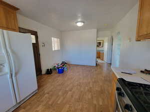 Kitchen featuring stainless steel range with gas cooktop, white fridge with ice dispenser, a textured ceiling, and light hardwood / wood-style flooring