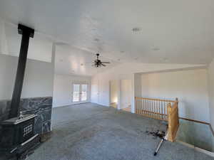 Unfurnished living room featuring a wood stove, french doors, vaulted ceiling, carpet flooring, and ceiling fan