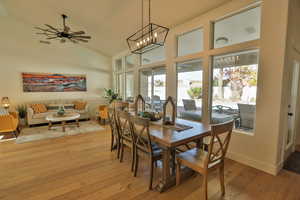 Dining room with light hardwood / wood-style flooring, ceiling fan with notable chandelier, and lofted ceiling