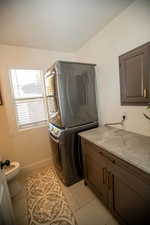 Clothes washing area with light tile patterned floors and stacked washer and clothes dryer