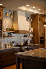 Kitchen with stone counters, wall chimney exhaust hood, dark wood-type flooring, stainless steel appliances, and pendant lighting