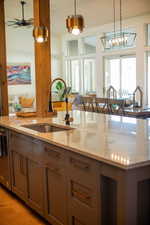 Kitchen with light stone countertops, ceiling fan with notable chandelier, decorative light fixtures, light hardwood / wood-style flooring, and dishwasher