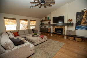 Living room featuring hardwood / wood-style floors, ceiling fan, a stone fireplace, and lofted ceiling