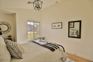 Bedroom with lofted ceiling, light wood-type flooring, and an inviting chandelier