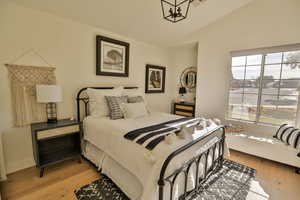 Bedroom with vaulted ceiling, an inviting chandelier, and light hardwood / wood-style flooring