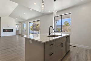 Kitchen with a center island with sink, sink, vaulted ceiling, light stone countertops, and light hardwood / wood-style floors