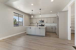 Kitchen with gray cabinetry, pendant lighting, a kitchen island with sink, appliances with stainless steel finishes, and light hardwood / wood-style floors