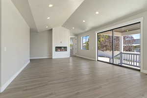 Unfurnished living room with a fireplace, a textured ceiling, vaulted ceiling, and light hardwood / wood-style flooring