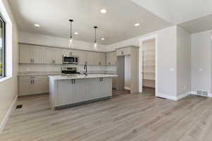 Kitchen featuring stainless steel appliances, light stone counters, light hardwood / wood-style flooring, gray cabinets, and a kitchen island with sink