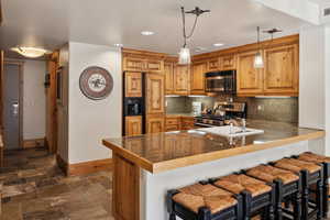 Kitchen with kitchen peninsula, a kitchen breakfast bar, backsplash, stainless steel appliances, and hanging light fixtures