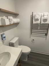 Bathroom with radiator heating unit, hardwood / wood-style flooring, toilet, and sink