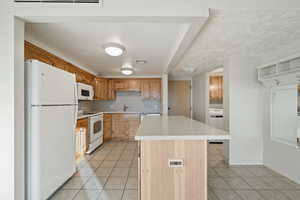 Kitchen featuring white appliances, sink, light tile patterned floors, a kitchen island, and washer / dryer