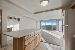 Kitchen with white refrigerator, light colored carpet, a textured ceiling, and light brown cabinets