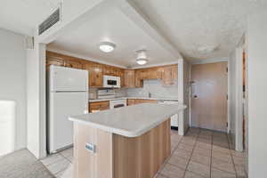 Kitchen with a center island, white appliances, a textured ceiling, and light tile patterned floors