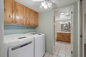 Clothes washing area with ceiling fan, light tile patterned flooring, cabinets, and independent washer and dryer