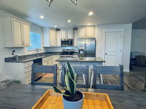 Kitchen with appliances with stainless steel finishes, sink, hardwood / wood-style flooring, dark stone countertops, and a center island