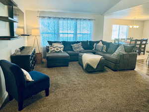 Living room with a textured ceiling, ceiling fan with notable chandelier, carpet floors, and lofted ceiling