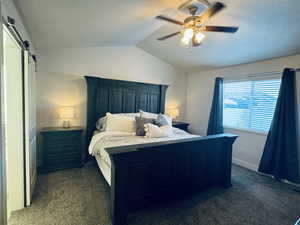 Primary bedroom with carpeted bedroom featuring a barn door, ceiling fan, and vaulted ceiling