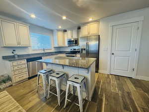 Kitchen featuring dark hardwood / wood-style flooring, a center island, dark stone countertops, and appliances with stainless steel finishes