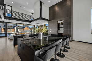 Kitchen featuring a breakfast bar, dark stone counters, a towering ceiling, a large island, and light hardwood / wood-style floors