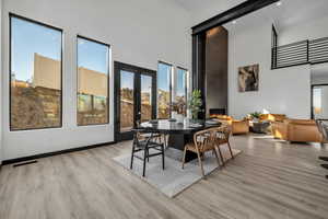 Dining room with a high ceiling, a large fireplace, light hardwood / wood-style flooring, and french doors